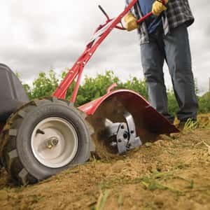 Man plowing a field using a gas powered tiller
