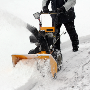 Yellow snow blower pushed by a man during snowfall